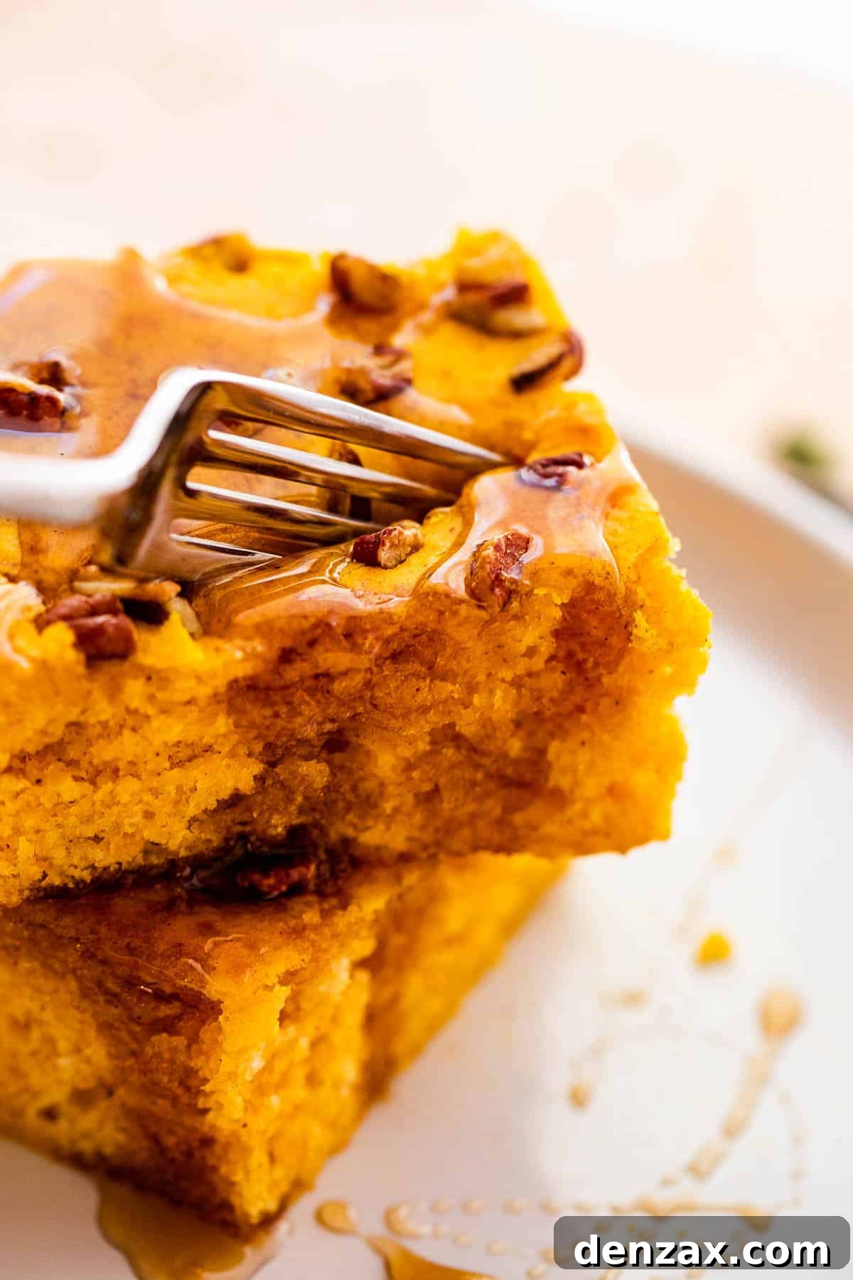 A fork piercing into a fluffy square of sheet pan pumpkin pancake, revealing its moist interior, with a light drizzle of syrup.