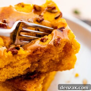 A fork cutting into a golden-brown sheet pan pumpkin pancake, revealing its fluffy interior, adorned with a drizzle of maple syrup and a sprinkle of chopped pecans.