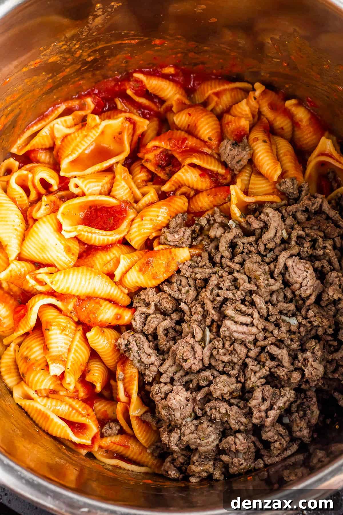 An overhead shot of an Instant Pot with cooked shells in sauce inside and a batch of browned ground beef added.