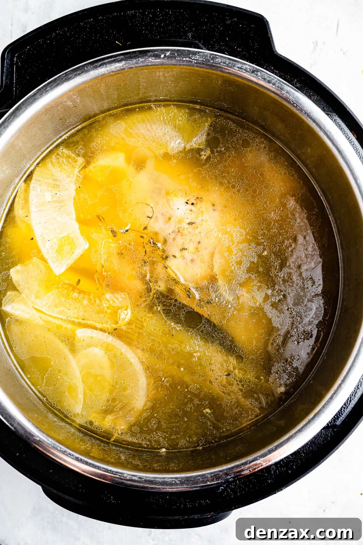 An overhead shot of the interior of an Instant Pot, filled with chicken broth, a cooked chicken, and scraps of vegetables.
