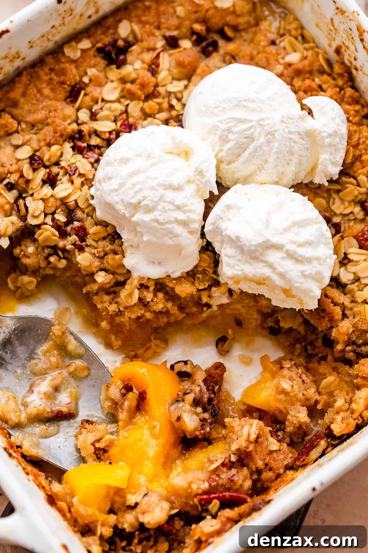 A pristine white baking dish filled with a golden-brown peach crisp, artfully adorned with several scoops of decadent vanilla ice cream, creating a mouthwatering dessert presentation.