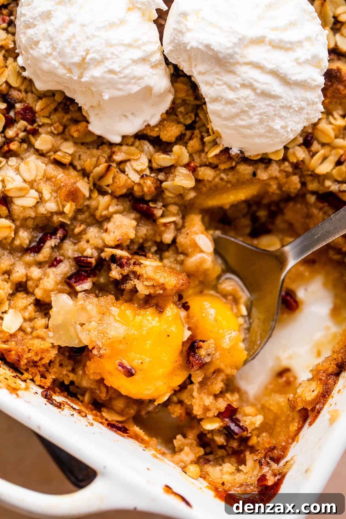 A beautiful peach crisp in a white baking dish, exquisitely topped with several scoops of rich vanilla ice cream, creating a perfect, comforting dessert.