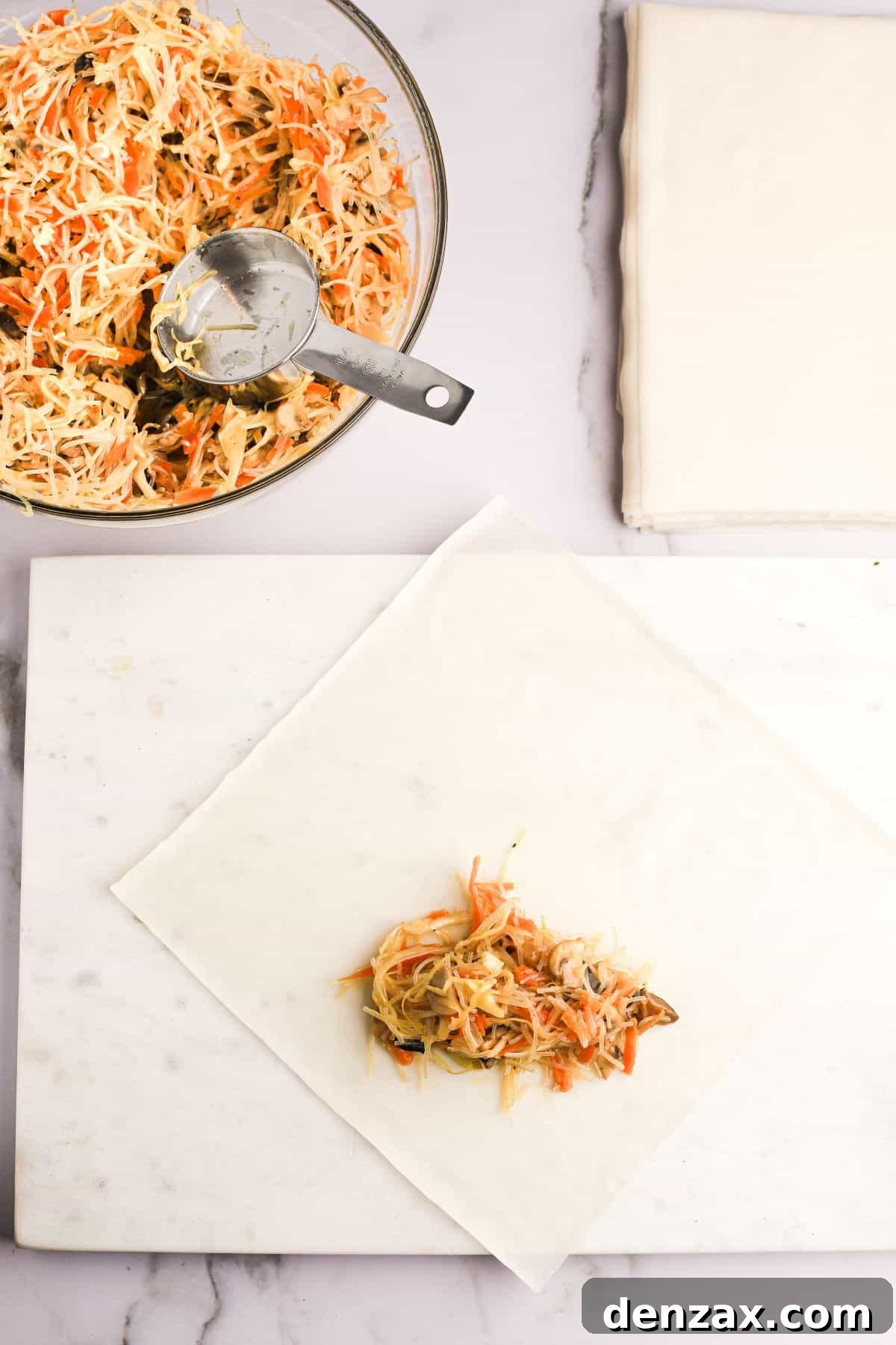 A spring roll wrapper laid out in a diamond shape on a cutting board, with a small portion of vegetable filling placed at the bottom corner, ready for folding.