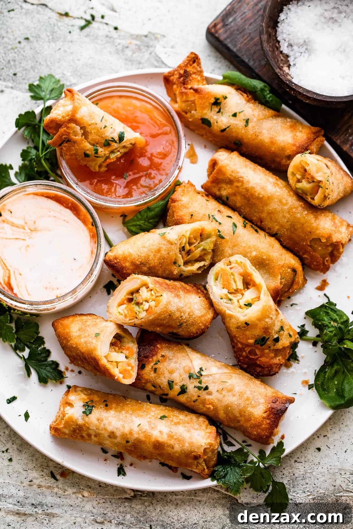 A beautifully presented plate of golden veggie spring rolls next to a small bowl of vibrant dipping sauce.