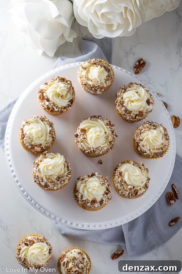 Close-up of fluffy carrot cake cupcakes with intricate cream cheese frosting swirls, garnished with pecans.