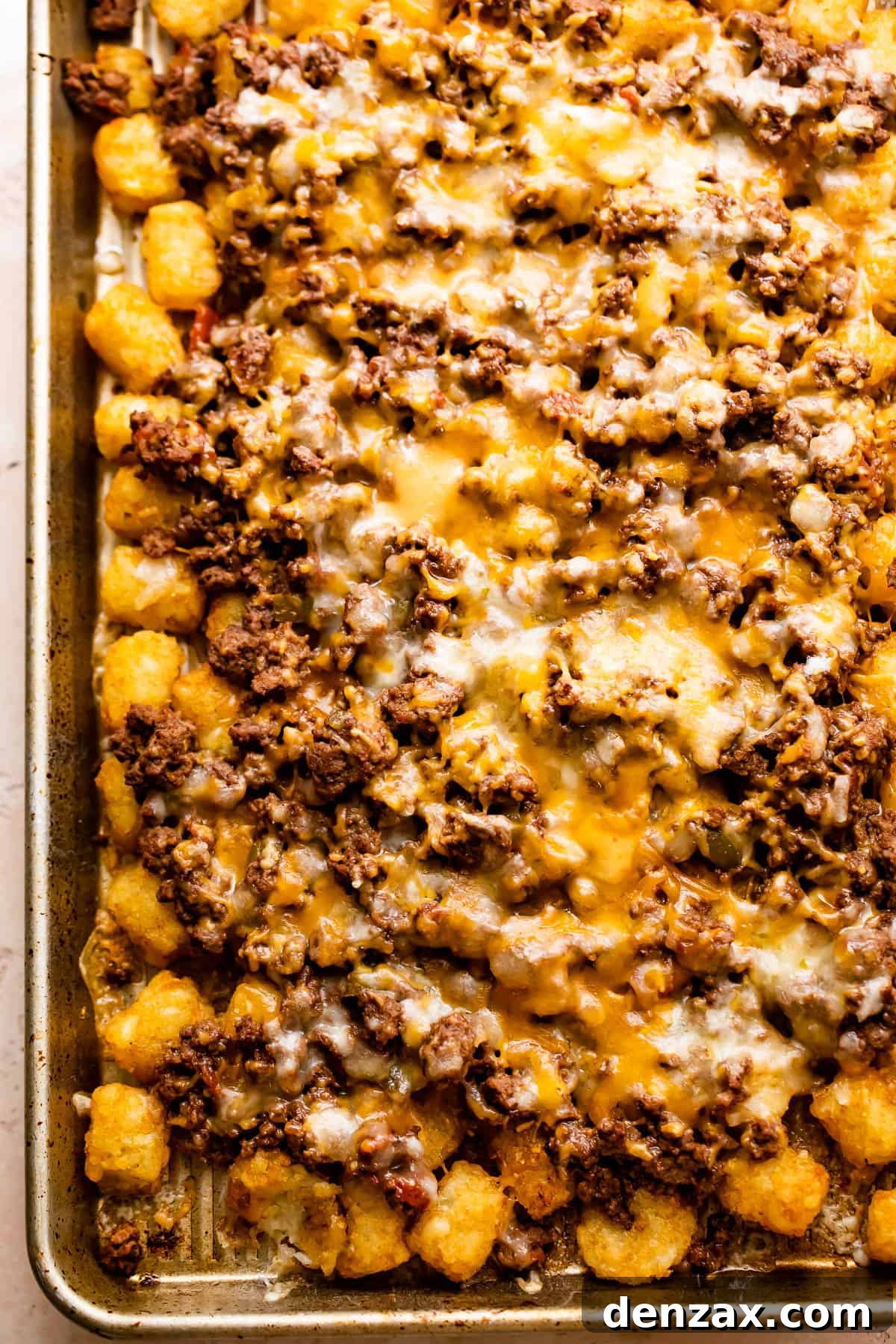A close-up shot of the sheet pan totchos immediately after baking, with the melted cheese still bubbling over the seasoned beef and crispy tater tots.