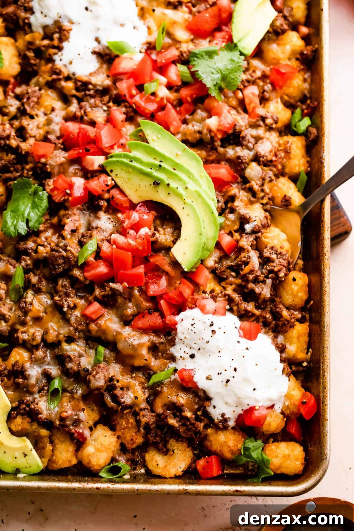 A vibrant platter of Sheet Pan Totchos with Beef, beautifully arranged with a variety of fresh toppings including diced tomatoes, creamy sour cream, and sliced avocados.