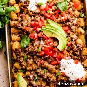 baking sheet with tater tots topped with ground beef, melted cheese, diced tomatoes, sour cream, and avocado slices