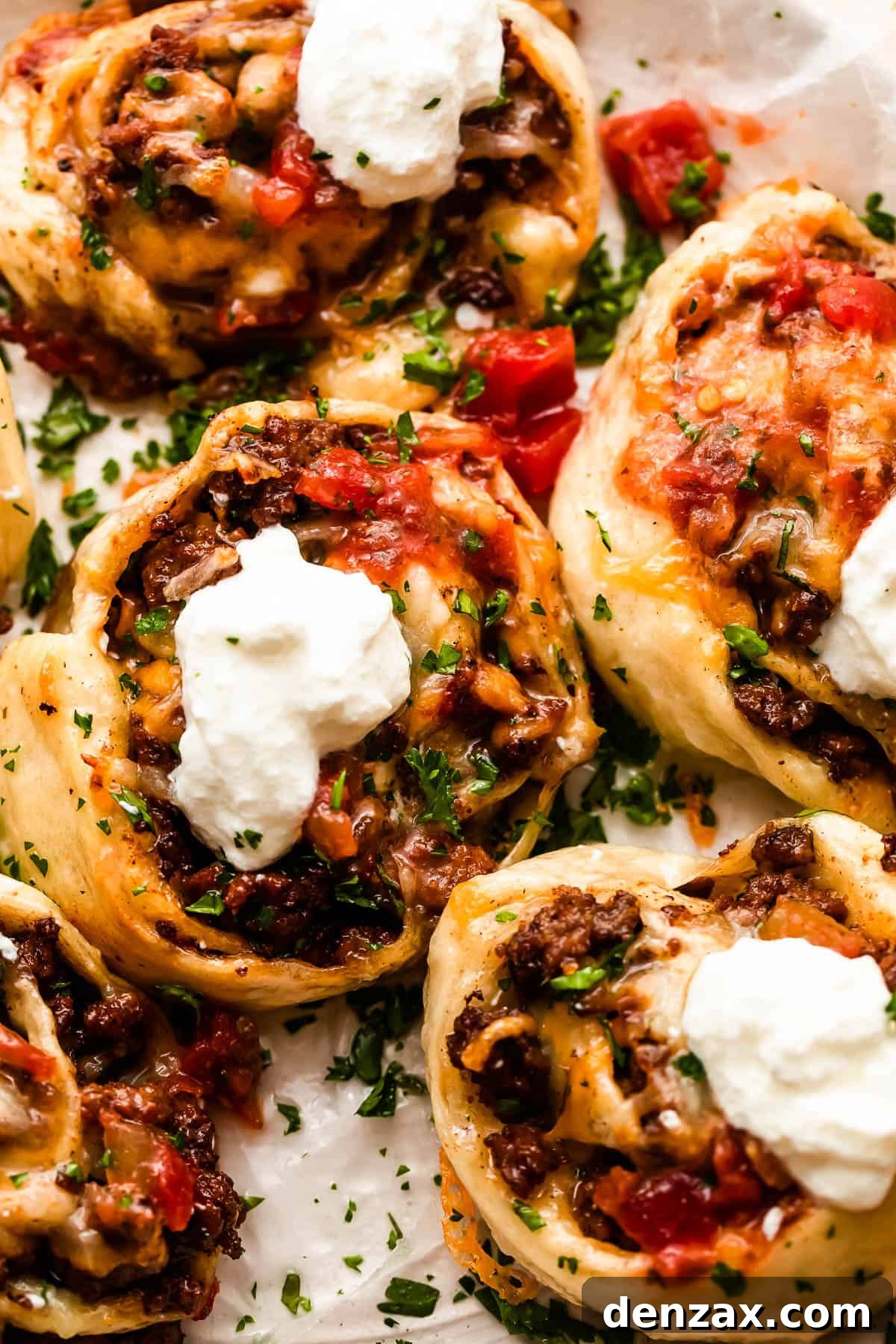 Overhead shot of freshly baked taco pinwheels garnished with diced tomatoes and a dollop of sour cream.