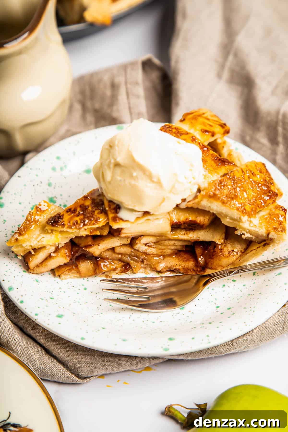 A golden-brown slice of homemade apple pie topped with melting vanilla ice cream, served on a white plate with a fork.