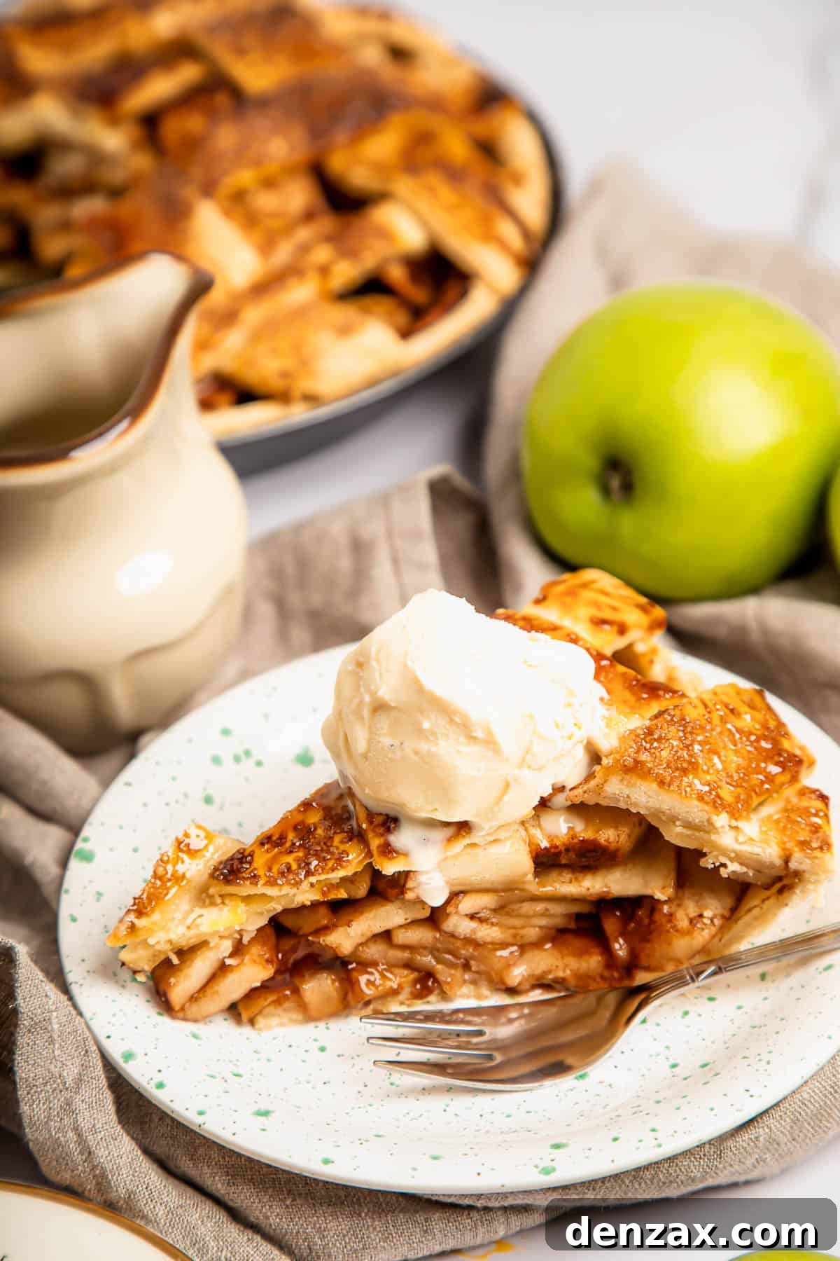 A close-up shot of a slice of warm apple pie, generously topped with a scoop of melting vanilla ice cream, served on a plate with a fork nearby.