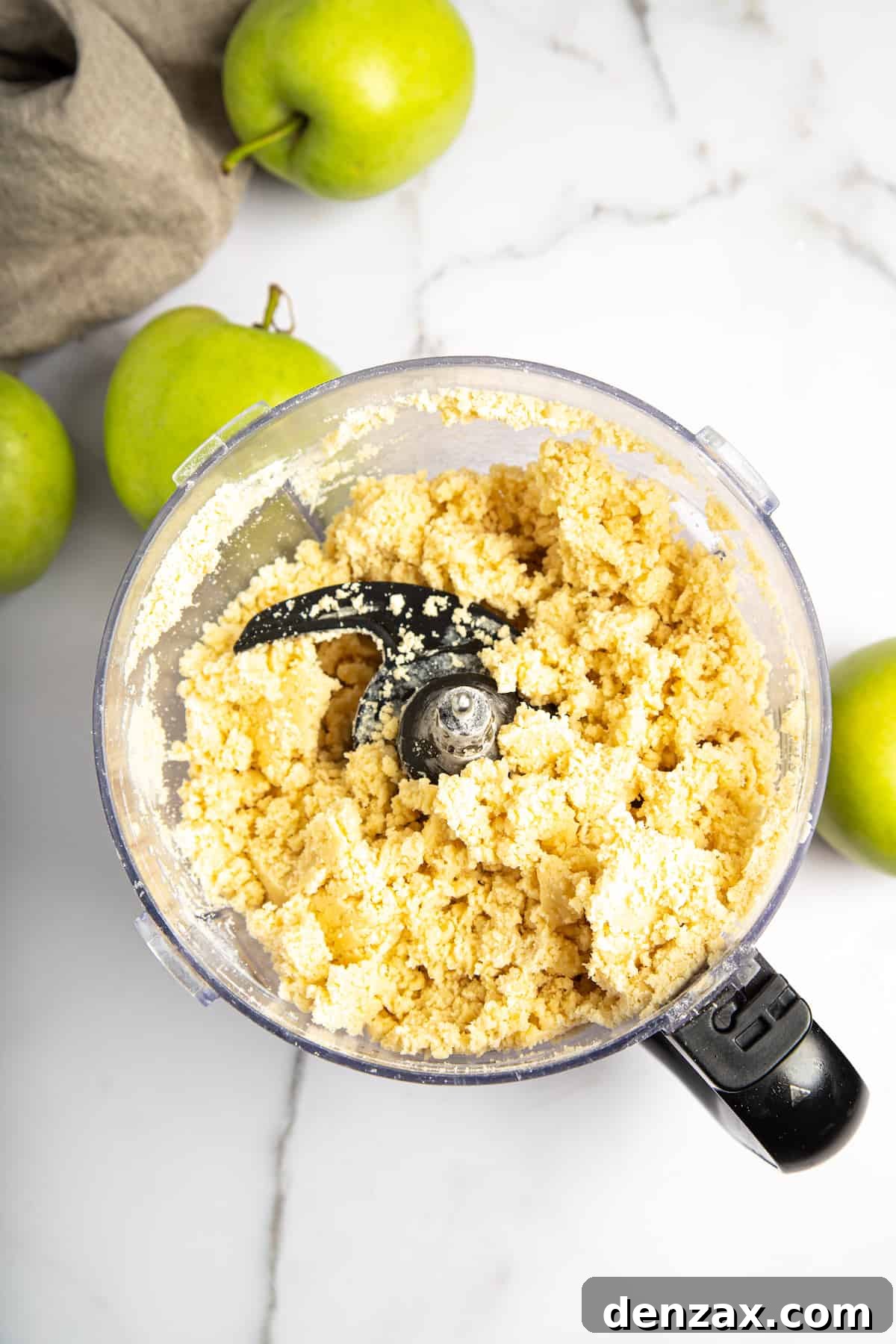 Pie crust dough being prepared in a food processor, showing a crumbly texture.