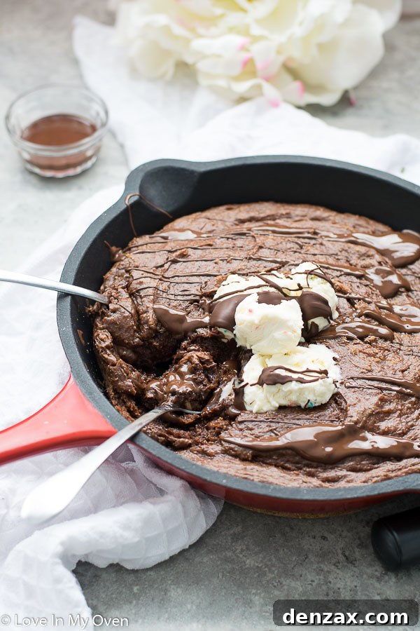 Gluten-Free Skillet Brownies freshly baked in a cast iron skillet, topped with ice cream and caramel sauce.