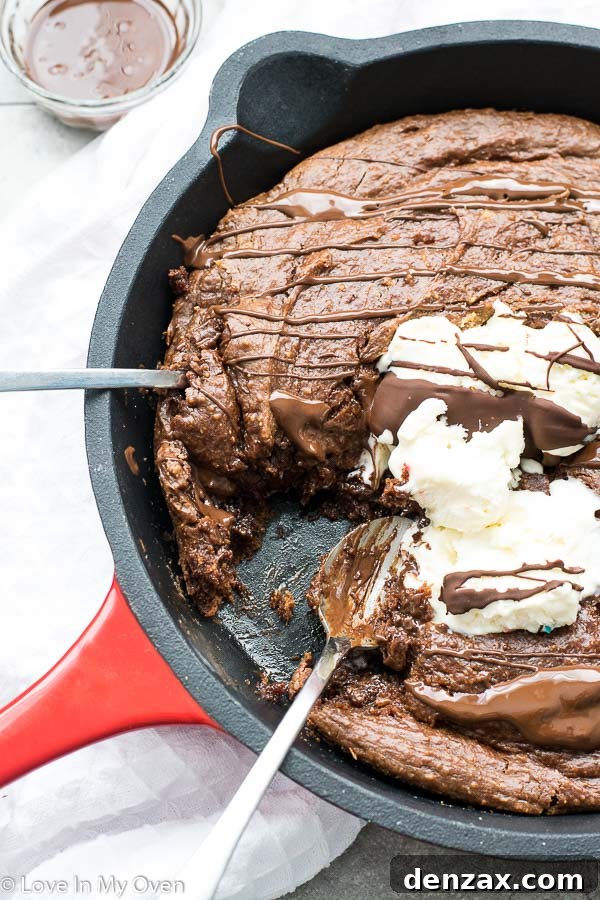 A slice of gluten-free skillet brownie on a plate, showing the fudgy inside, with ice cream and caramel.