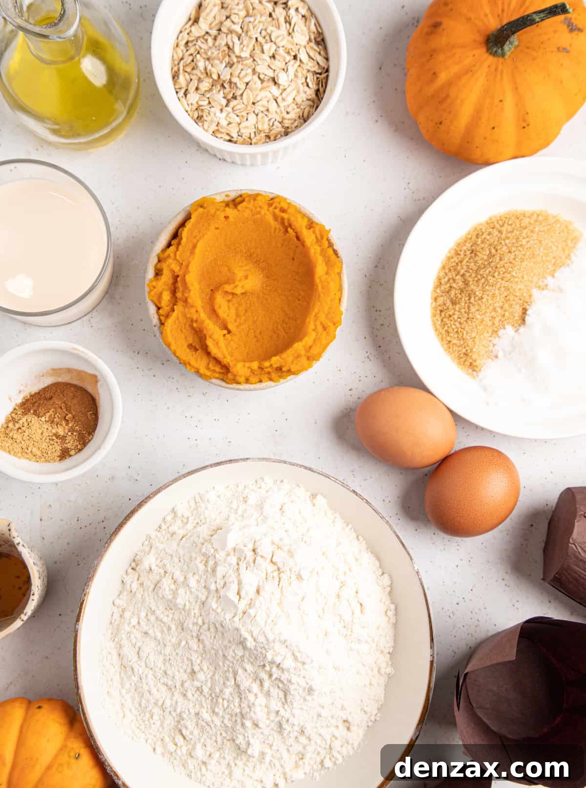 An overhead shot showcasing the key ingredients for homemade pumpkin muffins and their cinnamon crumble topping, including oats, sugar, eggs, flour, spices, sour cream, honey, and melted butter, arranged invitingly.