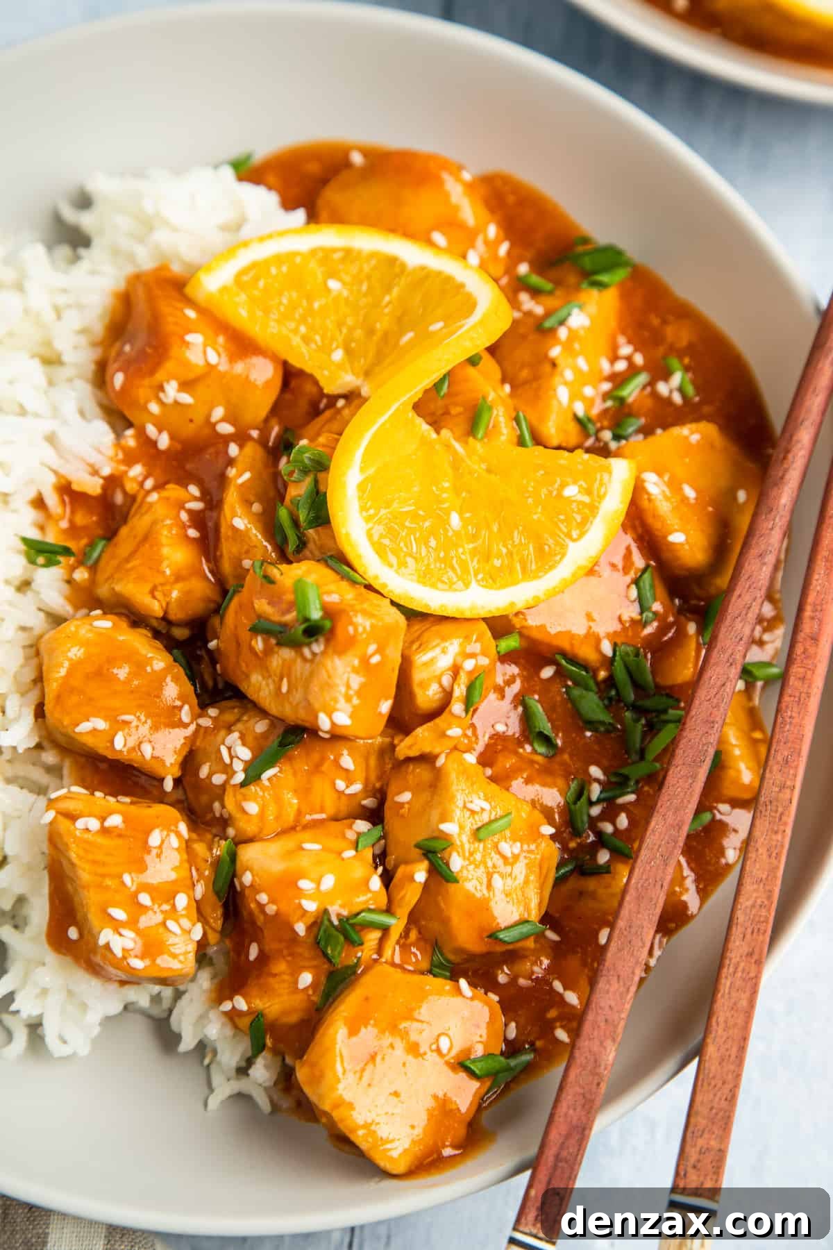 Overhead shot of orange chicken on a plate, garnished with an orange twist.