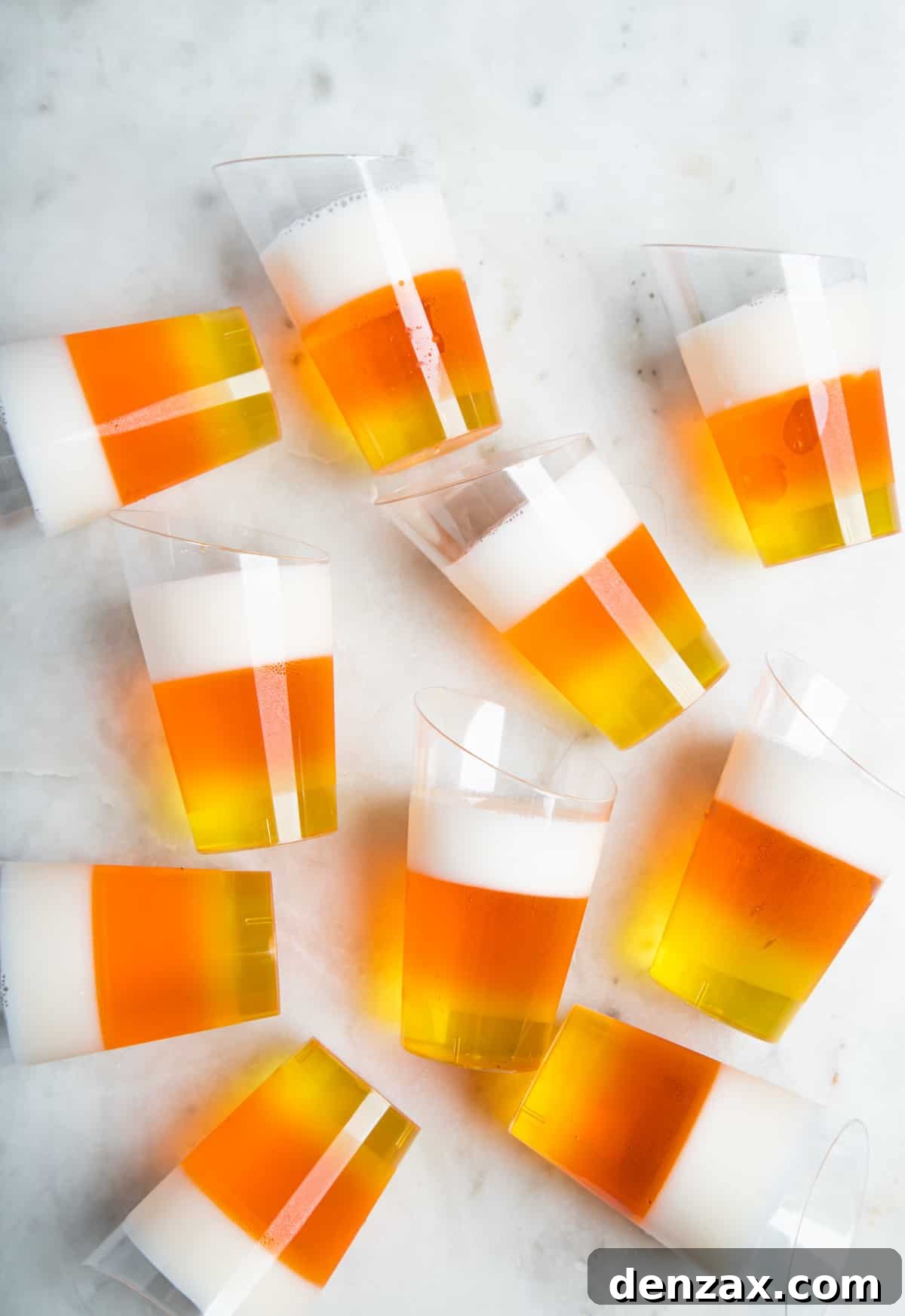 10 candy-corn jello shots scattered on a white table.