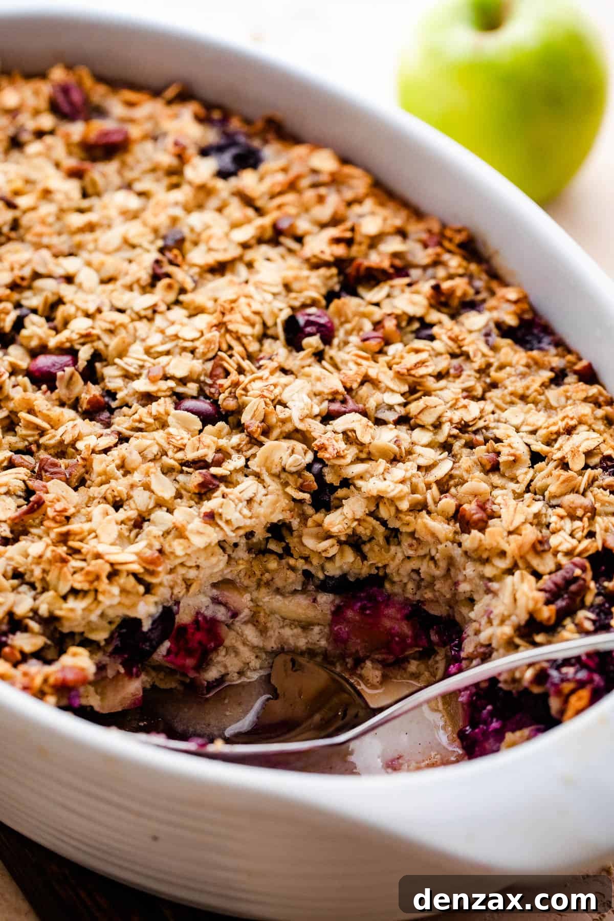 a white baking dish with baked oatmeal filled with apples and studded with blueberries.