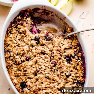 overhead shot of baked oatmeal in a white oval baking dish with a green apple set on the side, and a plate with oatmeal right above it.