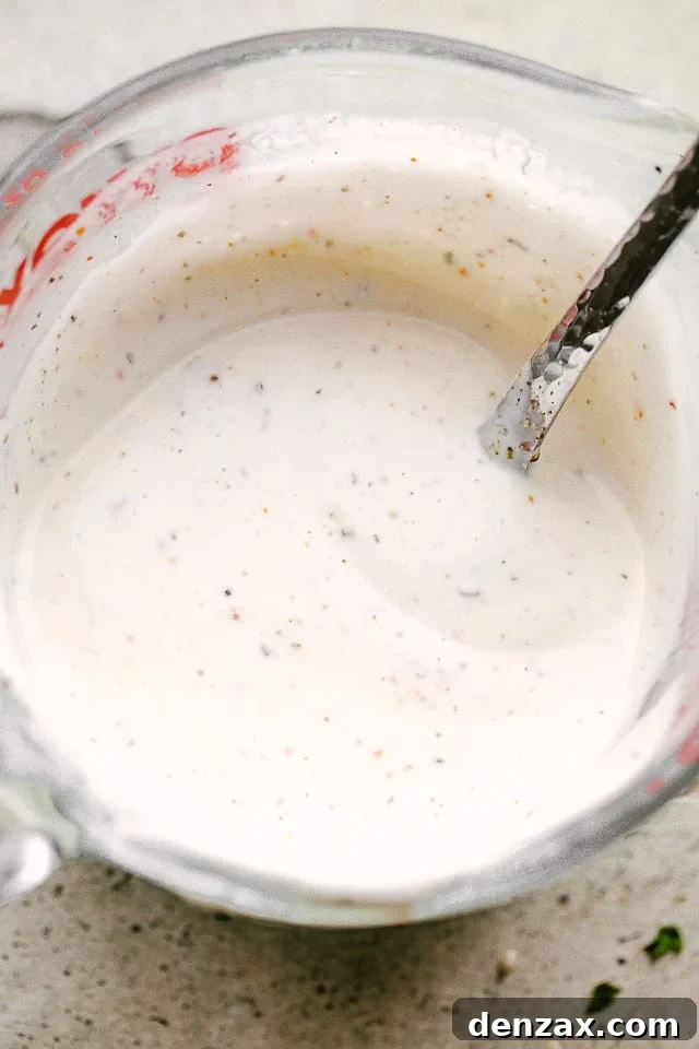 A mayonnaise-based dressing for Salmon BLT salad in a mixing cup with a spoon, highlighting its creamy texture.
