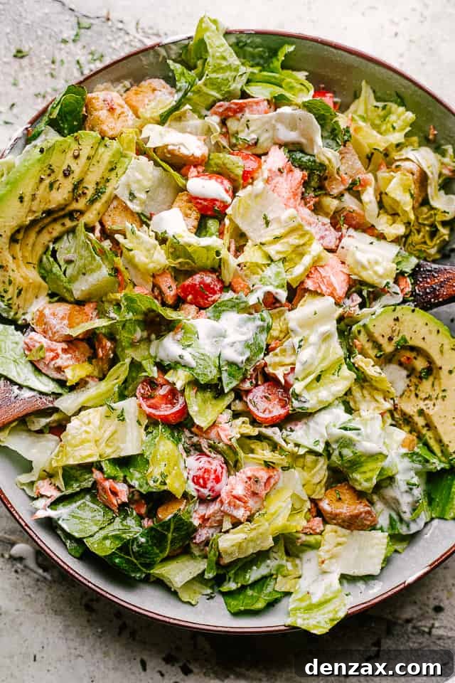Salmon BLT salad plated with dressing mixed throughout, ready for a delicious meal.