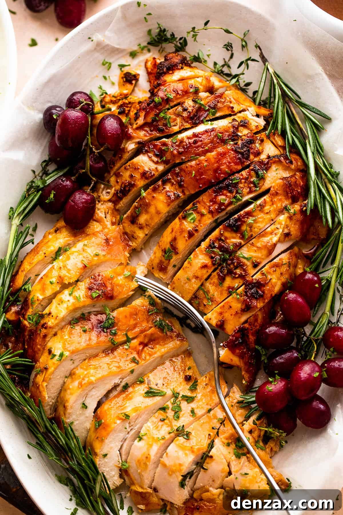A vibrant platter featuring two roasted turkey breasts, artfully sliced and garnished with fresh rosemary and juicy grapes.