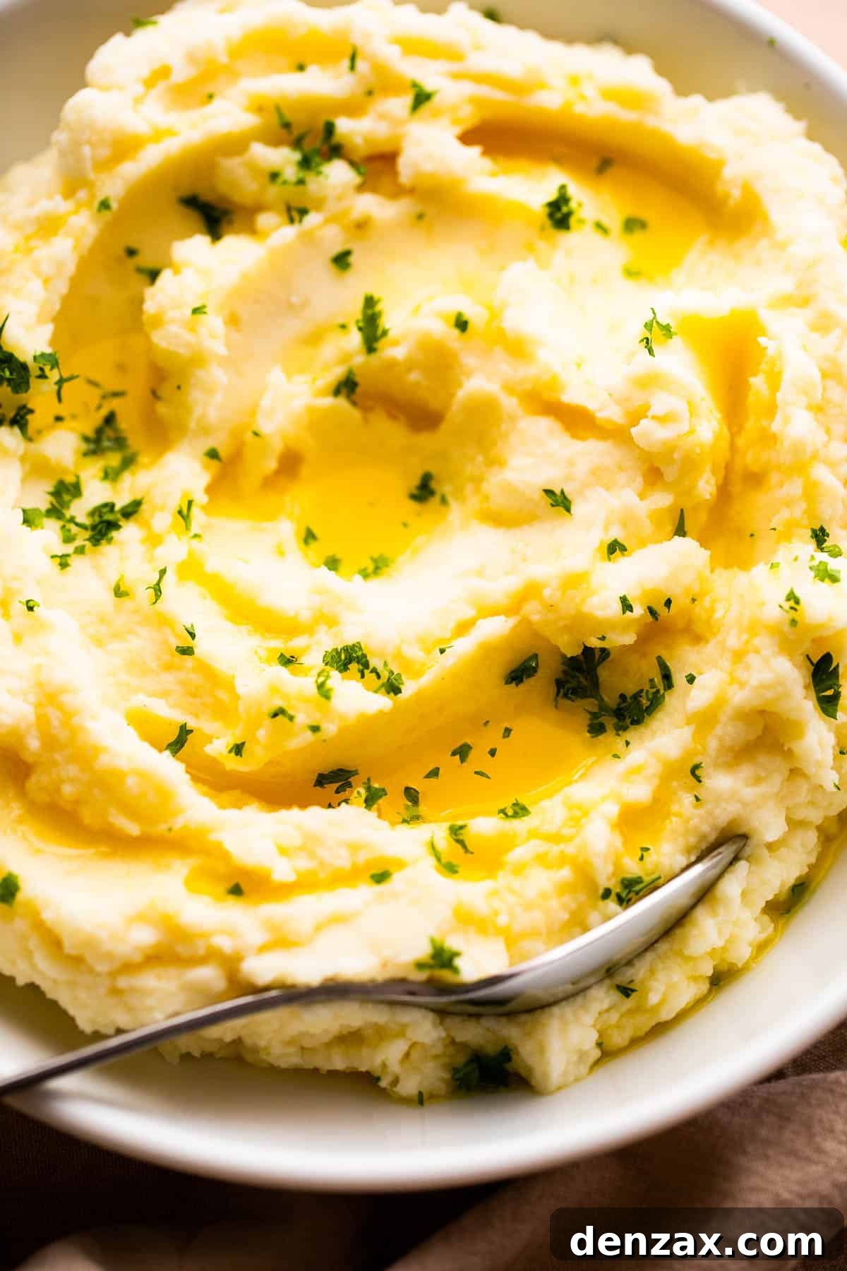 Close-up overhead shot of creamy mashed potatoes generously garnished with melted butter and fresh parsley, ready to be served.