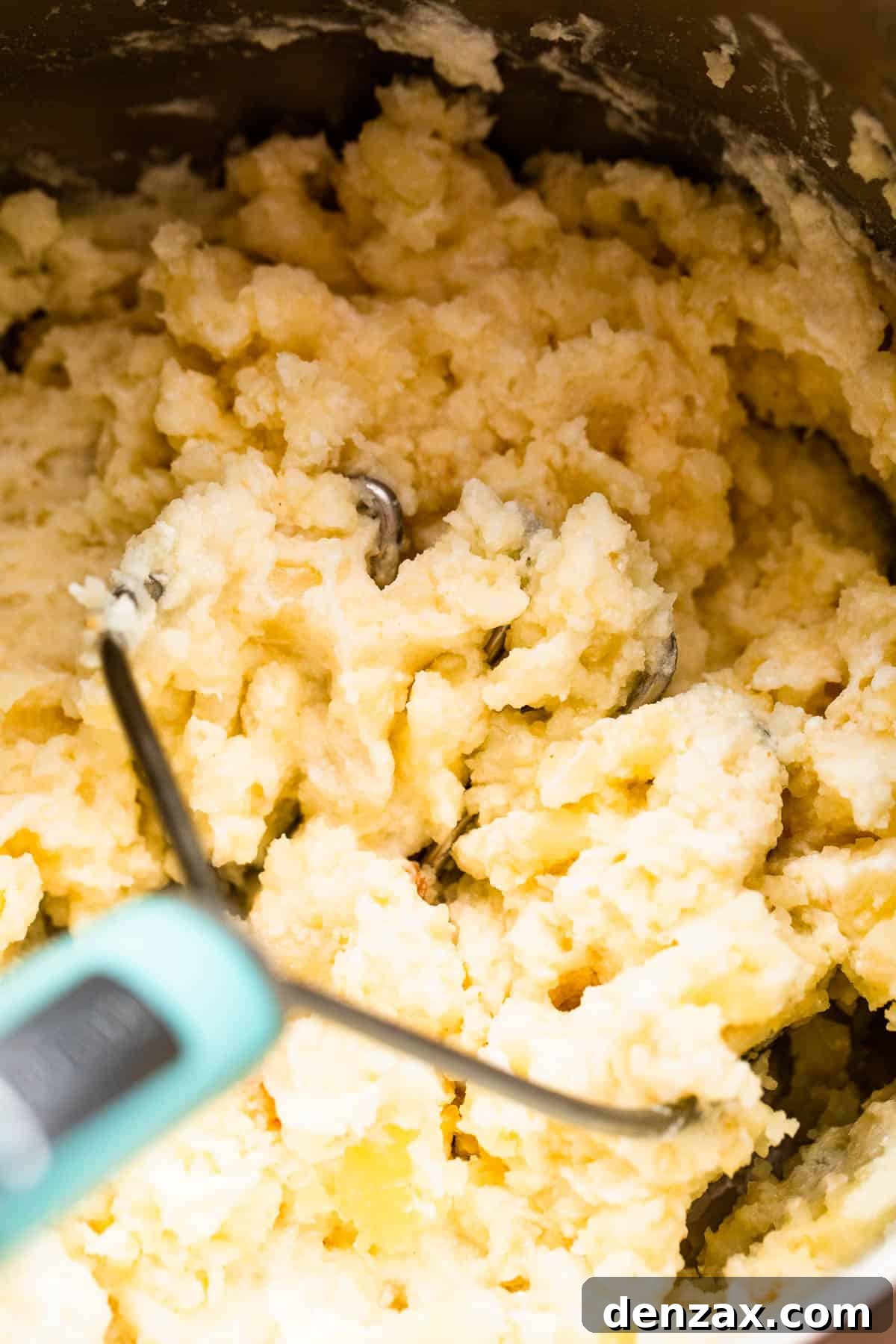 A close-up shot of a hand using a potato masher to create creamy mashed potatoes in a large pot.