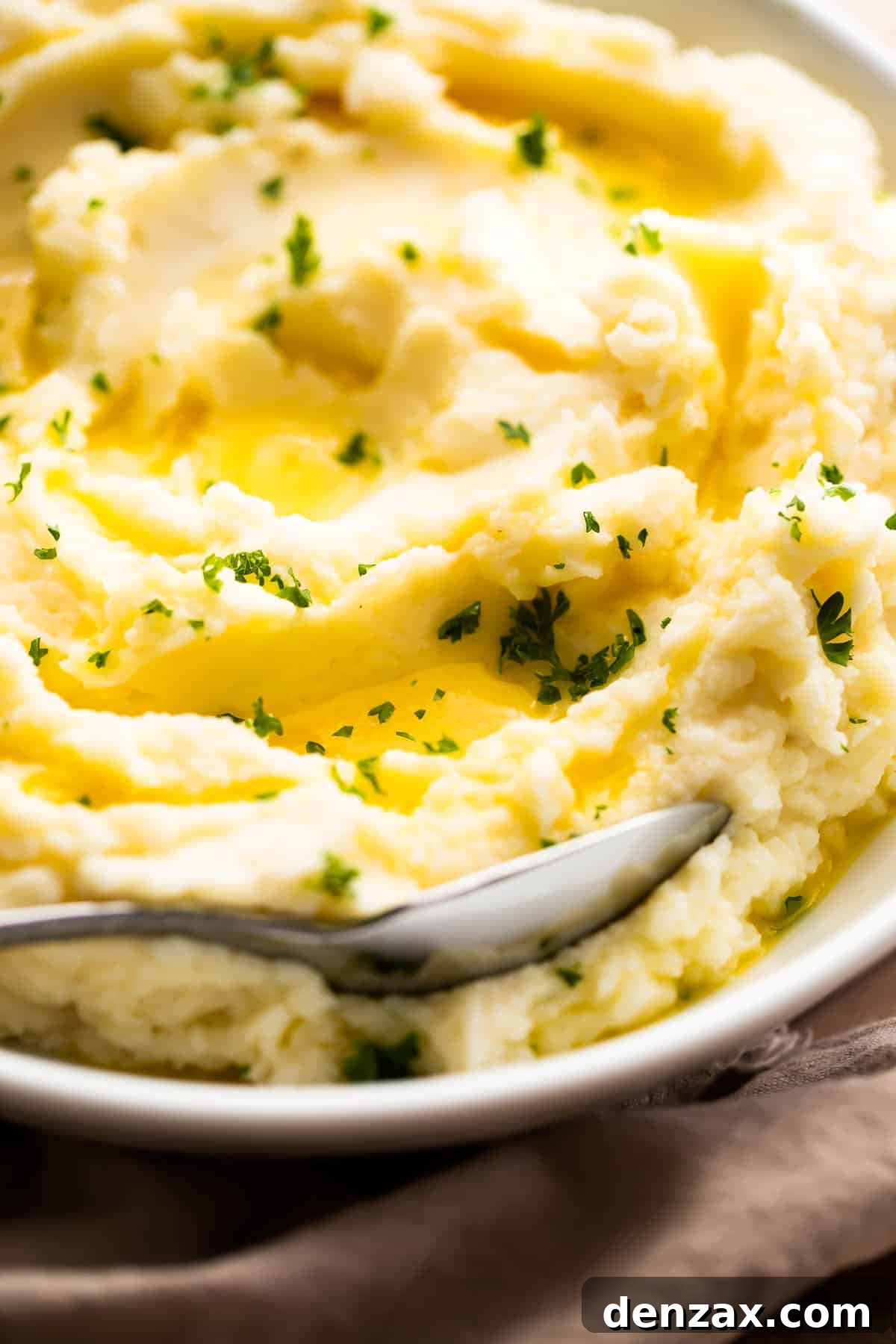 Close-up side shot of a bowl of creamy mashed potatoes, artfully garnished with melted butter and fresh parsley.