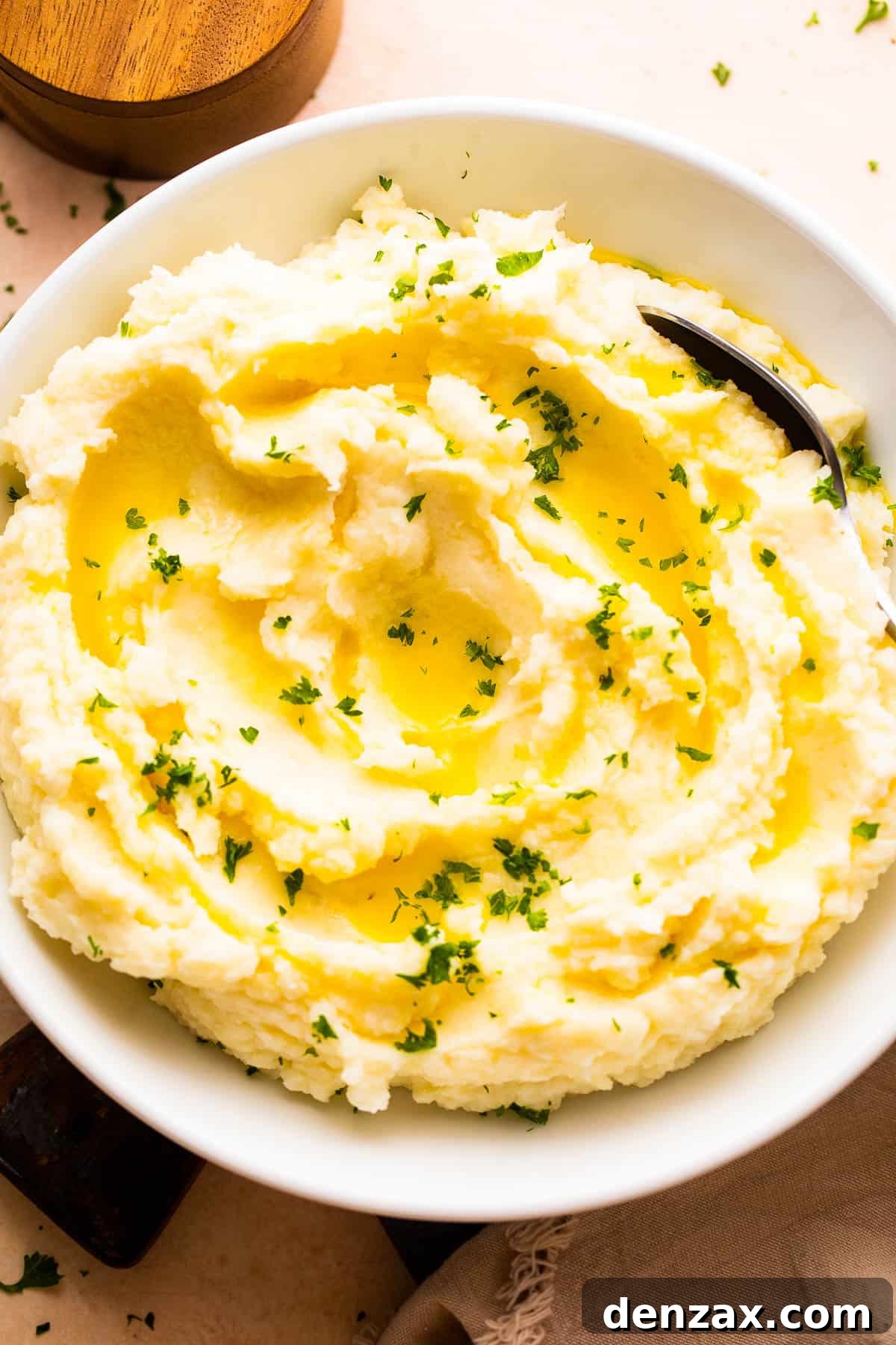 Overhead shot of a rustic bowl filled with creamy mashed potatoes, garnished with a swirl of melted butter and chopped fresh parsley.