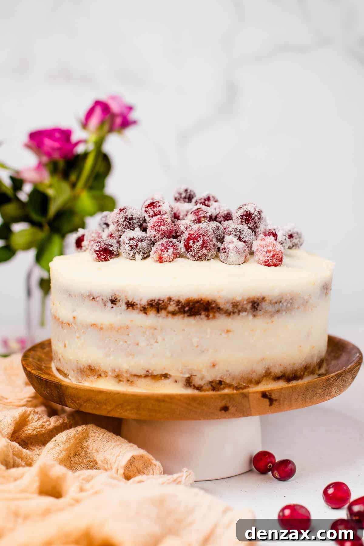 An assembled and iced cranberry carrot cake on a cake stand, beautifully topped with sparkling sugared cranberries, ready to be served.