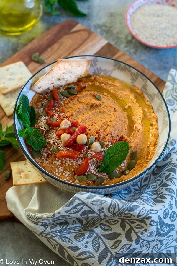 Bowl of roasted red pepper hummus garnished with fresh herbs and olive oil