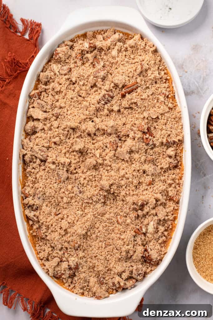 An unbaked Sweet Potato Casserole in a baking dish, beautifully topped with a generous layer of pecan streusel, ready to go into the oven.
