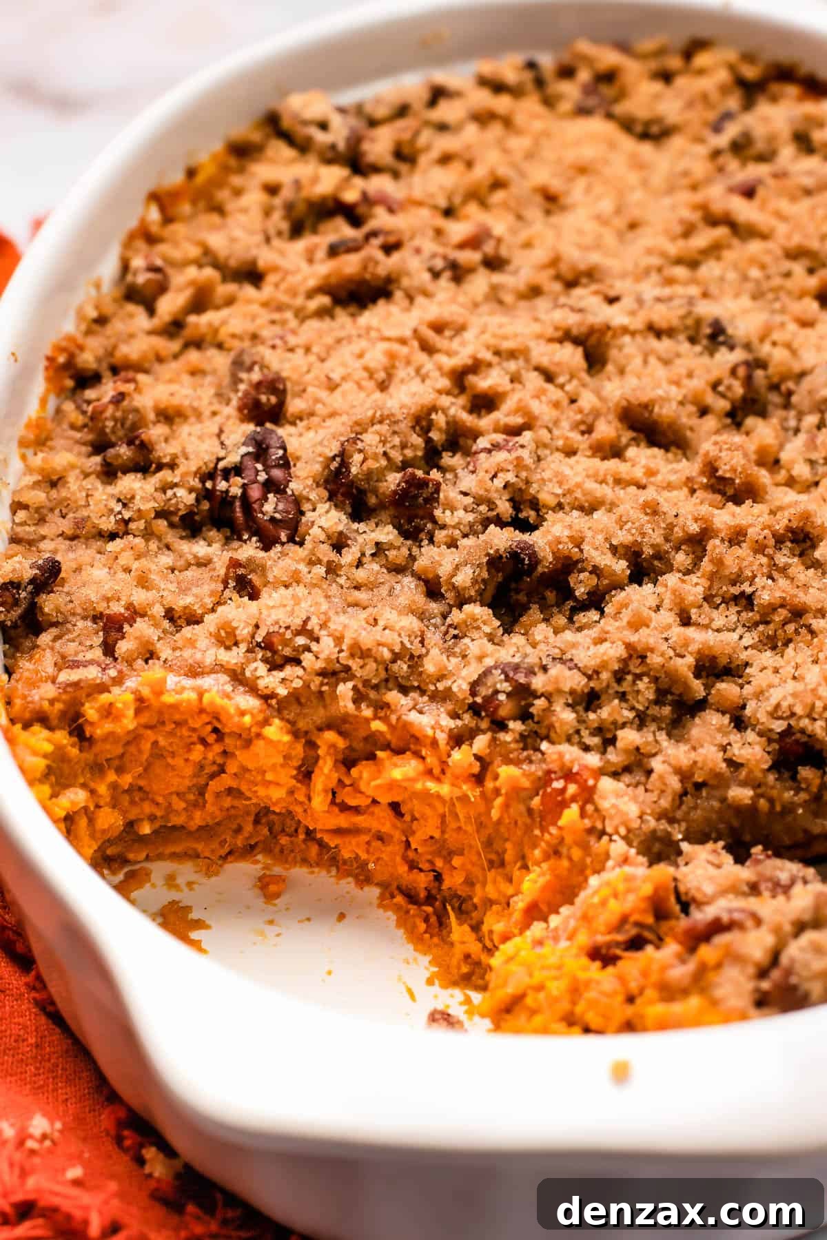 A close-up side view of a baked Sweet Potato Casserole in a baking dish, revealing its distinct layers of creamy sweet potato and crunchy pecan streusel topping.