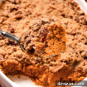 A shot of the sweet potato casserole with a serving spoon lifting a portion out of the dish, showing the texture of the baked casserole mixture and crumb topping.
