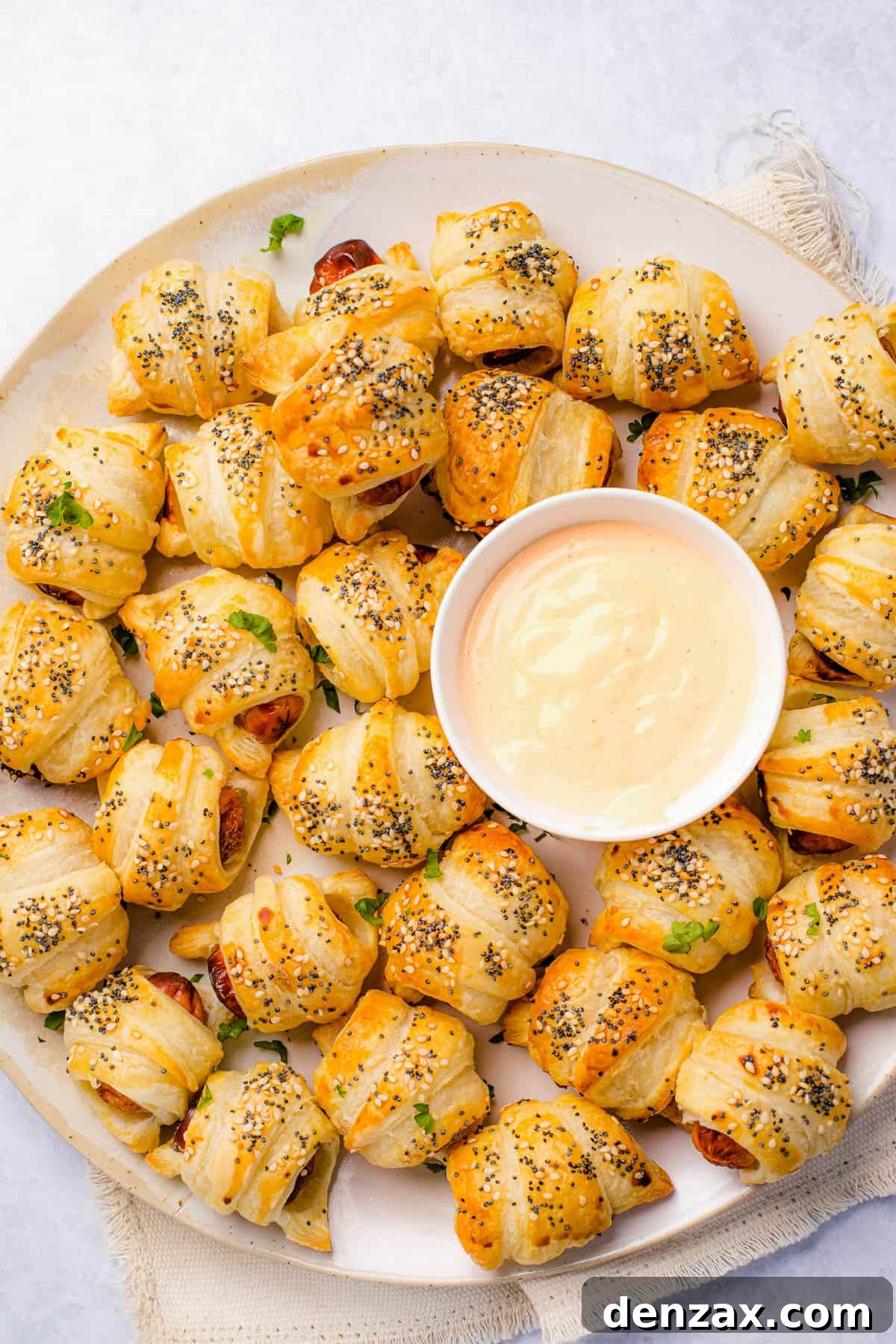 A platter of pigs in a blanket with a bowl of dipping sauce in the center.