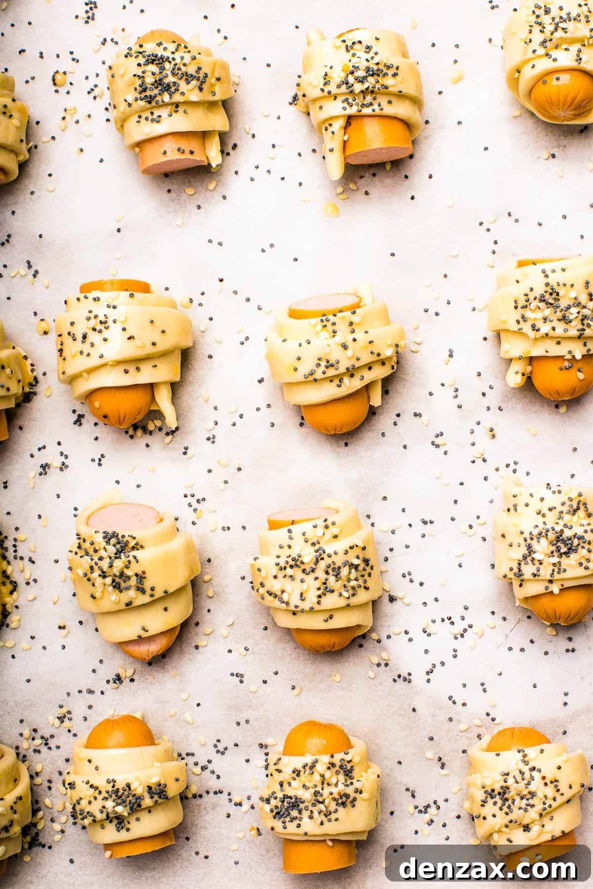 Unbaked pastries brushed with egg wash and sprinkled with sesame seeds and poppy seeds.