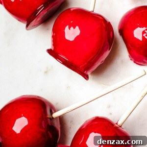 Several candy apples on a white cutting board. Plain Granny Smith apples and an orange fringed placemat in the background.