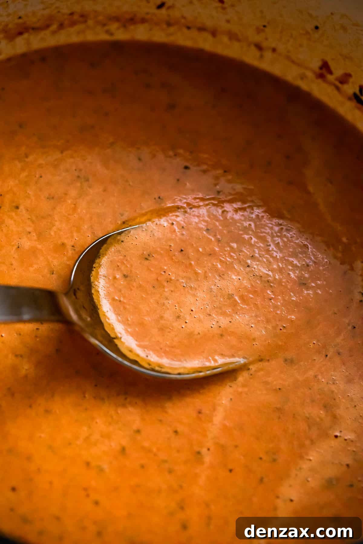 A ladle stirring through creamy roasted tomato basil soup inside a large, inviting soup pot, steam gently rising.