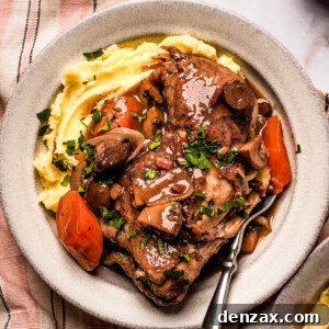 A serving of coq au vin with mashed potatoes on a stoneware plate.