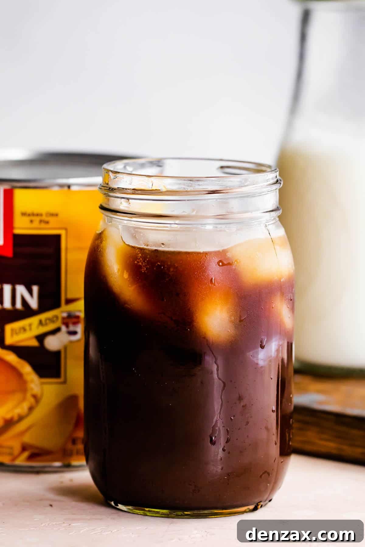 jar filled coffee and ice, with a pumpkin can placed right behind it.