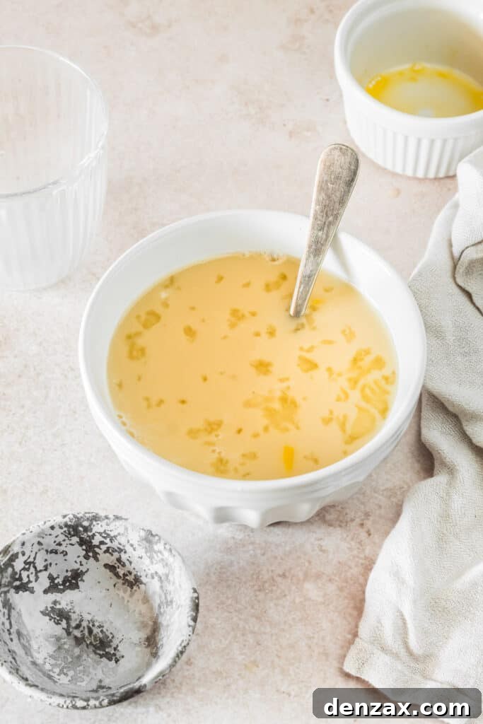 A small mixing bowl with egg, milk, yeast, and water mixed together. A floury spoon and dish towel are on the work surface.
