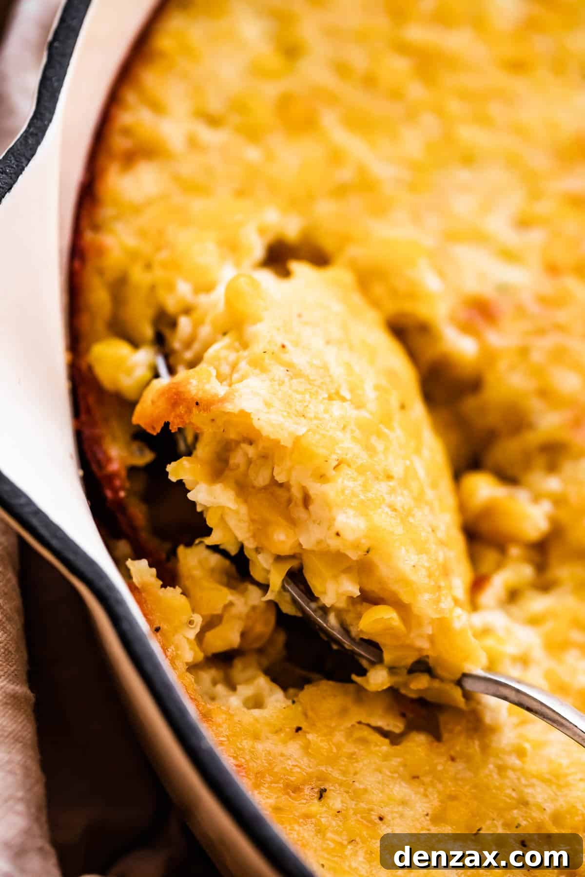Close-up shot of baked corn casserole in a white skillet with a spoon.