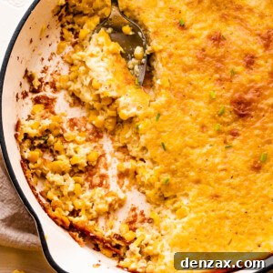 A spoon lifting a serving of creamed corn pudding from a white cast iron skillet.