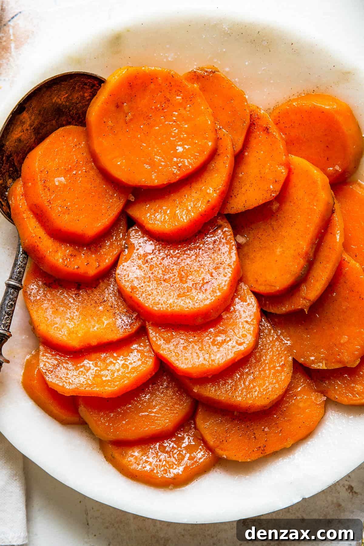 A white serving dish with sliced candied sweet potatoes and a serving spoon.