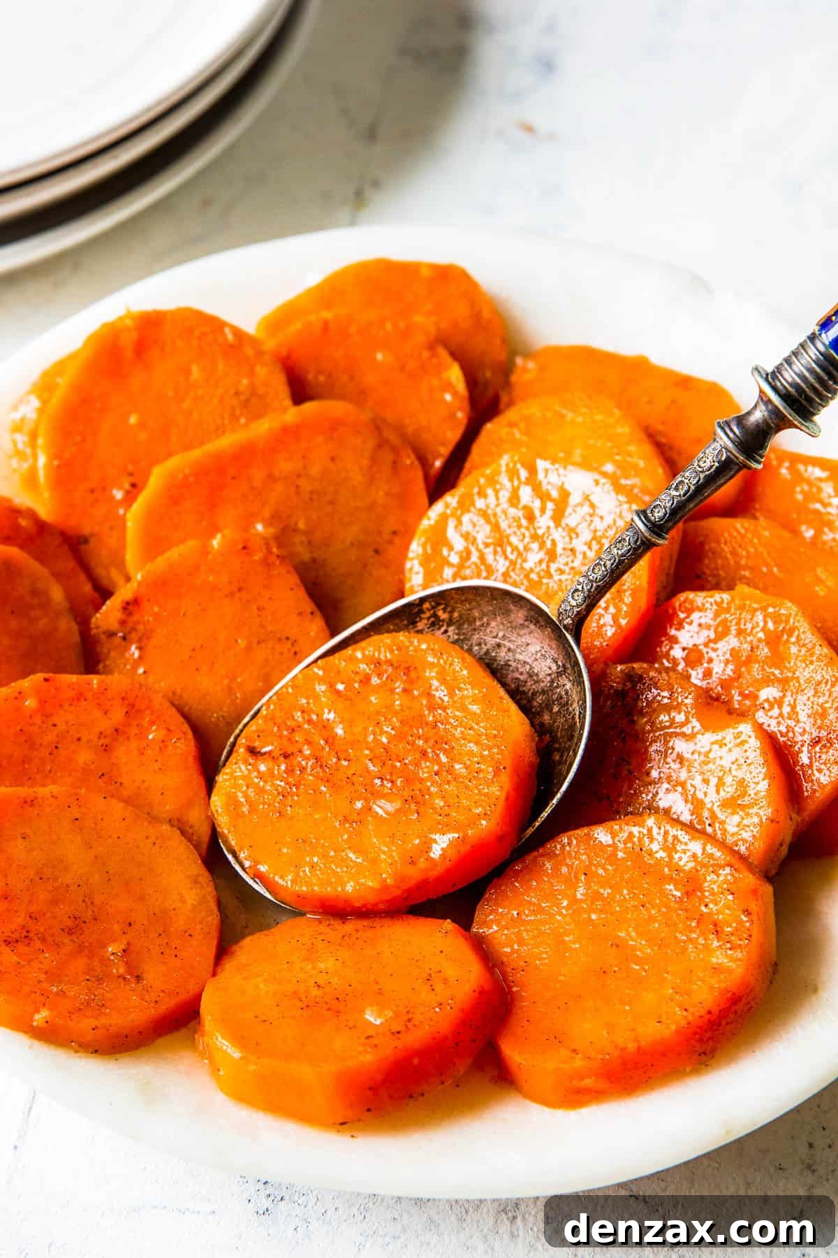 A white dish full of candied yams and a spoon.