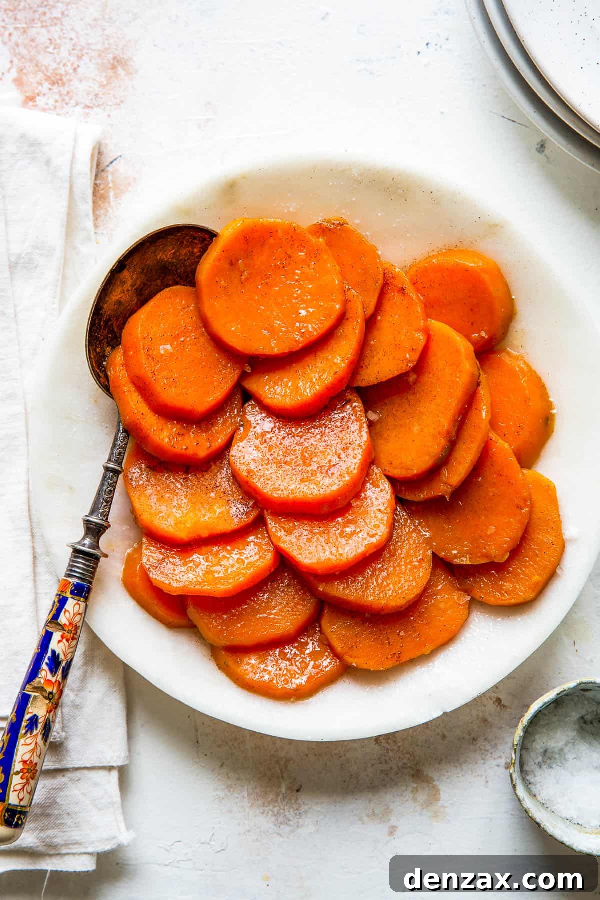 A white serving dish with sliced candied sweet potatoes and a serving spoon.
