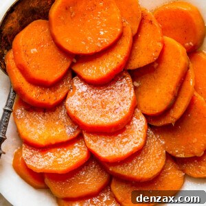 A white serving dish with sliced candied sweet potatoes and a serving spoon.