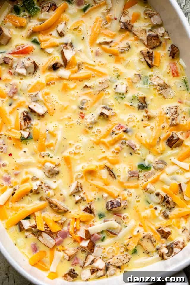 Peppers, onions, eggs, and cheese in a baking dish ready for the oven.