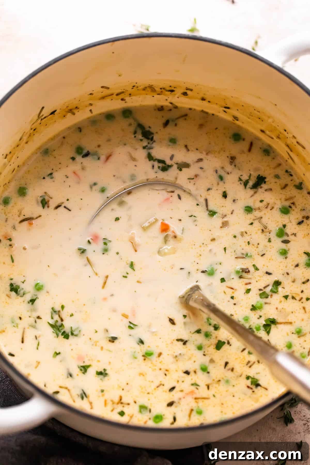 overhead shot of turkey pot pie soup in a white dutch oven with a ladle inside the pot.